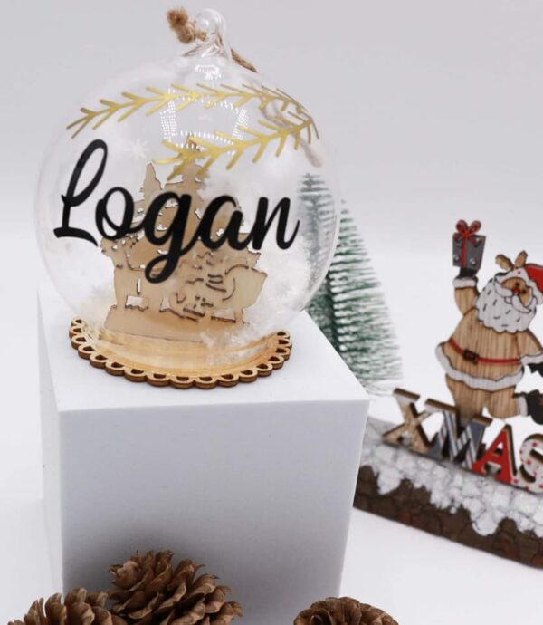 Boules de Noël sujet en bois en verre avec son décors et avec le prénom d'un membre de votre famille. Une belle idée de décoration pour son sapin.